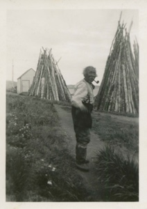 Image of Old Eskimo [Inuk] man with winter wood stacks beyond